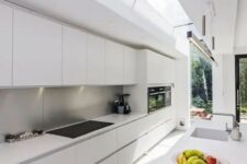 a long narrow minimalist white kitchen with a metal backsplash and skylights to bring much light in