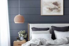 a lovely bedroom with a midnight blue beadboard accent wall, a white bed with black and white bedding, a stained nightstand