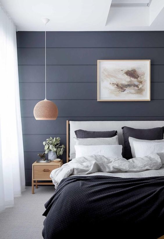 a lovely bedroom with a midnight blue beadboard accent wall, a white bed with black and white bedding, a stained nightstand