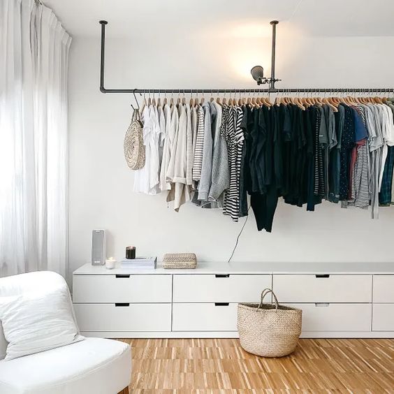 a lovely makeshift closet with a long railing for hanging clothes and a long white dresser to store smaller things
