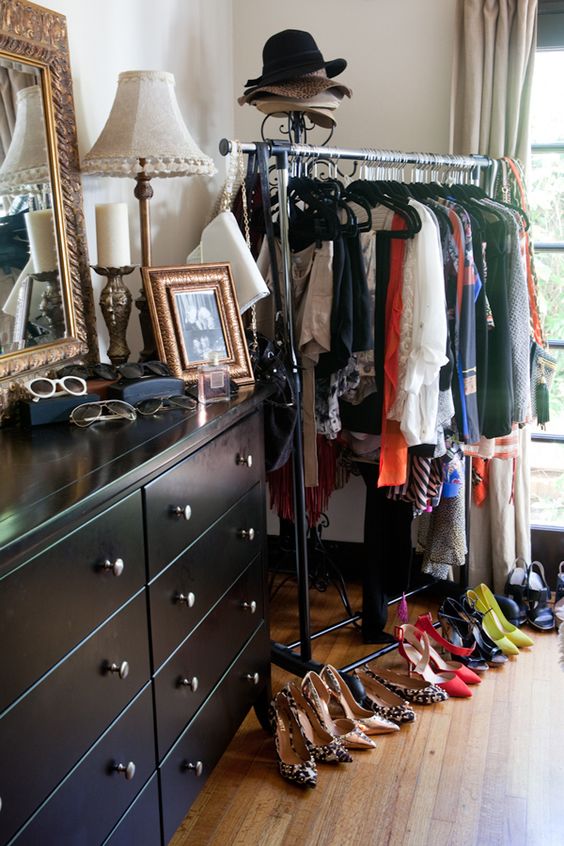 a makeshift closet with a black metal rack, a black dresser and some clothes, shoes and accessories on display