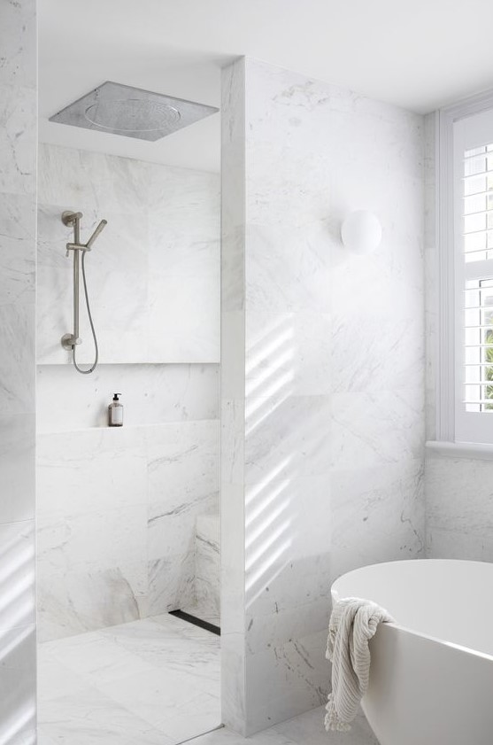 a minimalist bathroom clad with white marble tiles, a shower space and a bathtub is a chic space