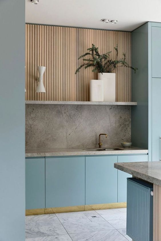 a minimalist kitchen with light blue and stained fluted cabinets, grey stone countertops and a backsplash, potted plants
