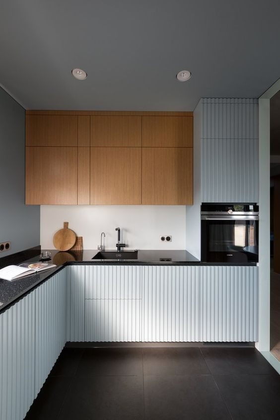 a minimalist kitchen with pale blue ridged cabinets and stained ones, black countertops and black fixtures