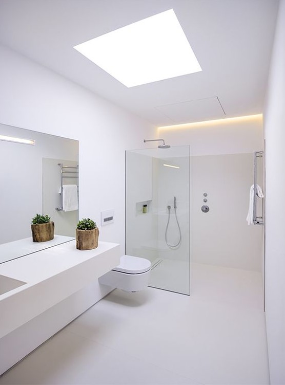 a minimalist white bathroom with a skylight, a floating vanity, a seamless glass shower space and built-in lights