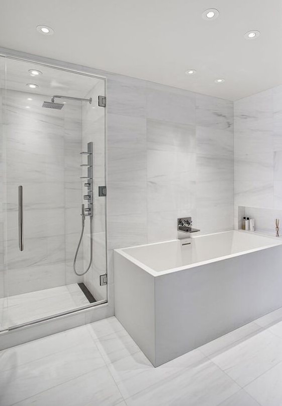 a minimalist white bathroom with marble large scale tiles, a square tub and built in lights all over