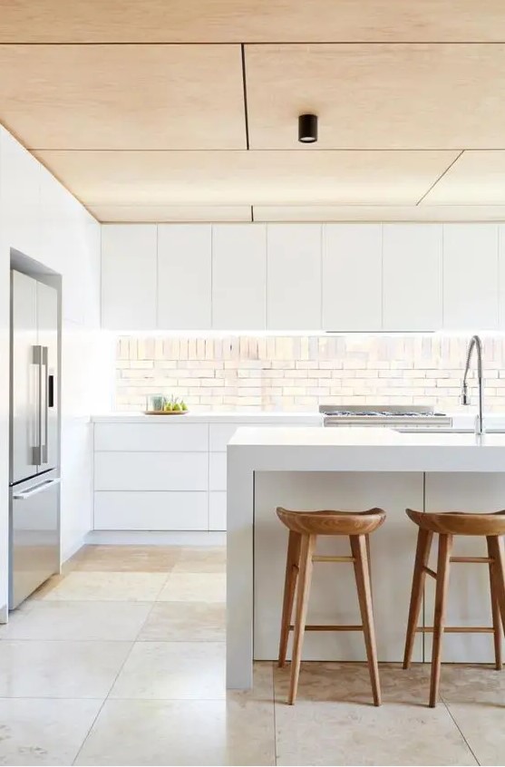 a minimalist white kitchen with a wooden ceiling, stools and an eye catchy backsplash