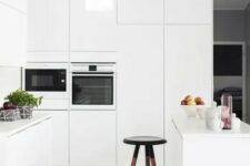 a minimalist white kitchen with no handles, a stool and tall cabinets to accomodate everything