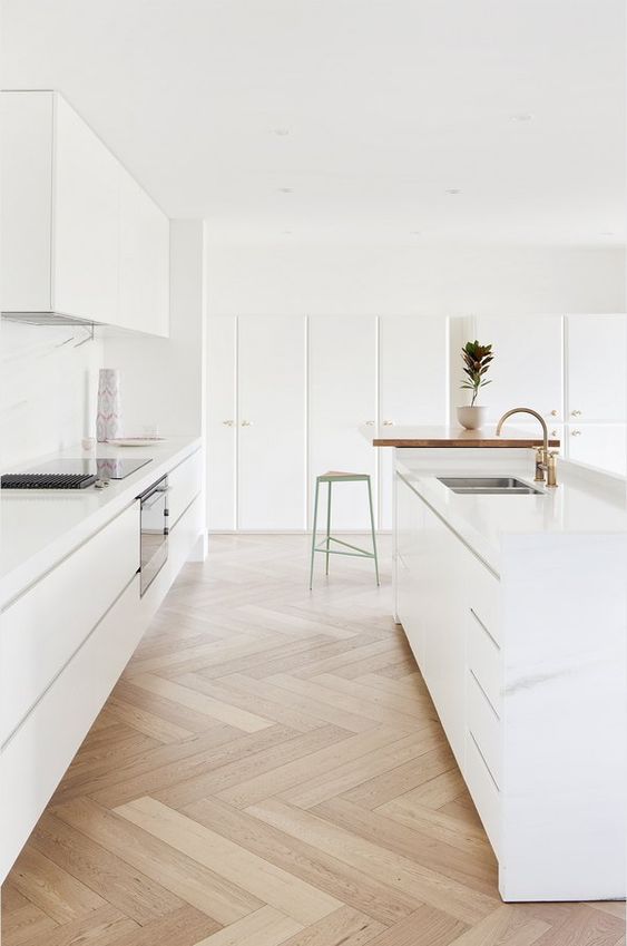 a minimalist white kitchen with sleek cabinetry, a large kitchen island, white countertops and a backsplash, gold fixtures