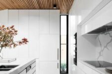 a minimalist white kitchen with sleek cabinets, a wooden ceiling and terrazzo floors plus a large skylight to maximize natural light