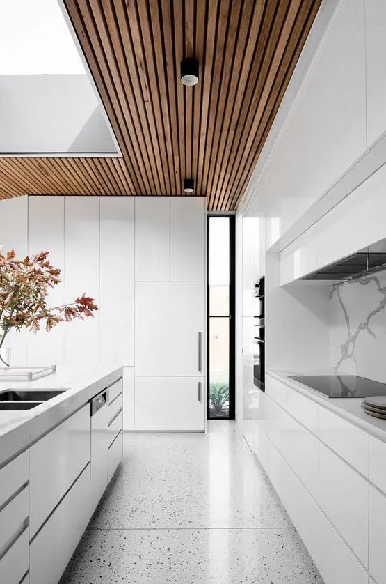 a minimalist white kitchen with sleek cabinets, a wooden ceiling and terrazzo floors plus a large skylight to maximize natural light