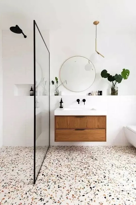 a modern bathroom in white, with a terrazzo floor, a wooden floating vanity and touches of gold