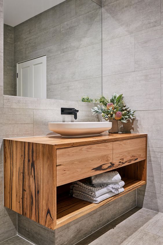 a modern bathroom with grey tiles, a floating timber vanity with drawers and a shelf, a cool sink and a black faucet