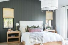 a modern farmhouse bedroom with a black beadboard wall, light stained furniture, much natural light and layered rugs
