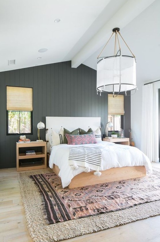a modern farmhouse bedroom with a black beadboard wall, light stained furniture, much natural light and layered rugs