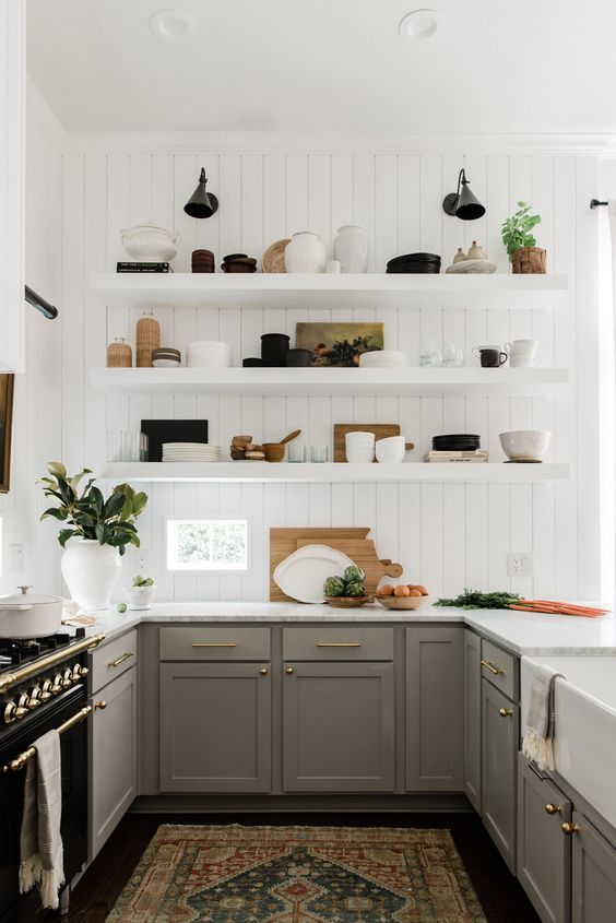 a modern farmhouse kitchen with green grey cabinets, open shelves, white stone countertops and black sconces