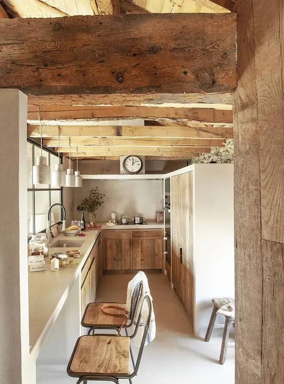 a modern farmhouse kitchen with rough wood cabinets and wooden beams, white stone countertops and pendant lamps