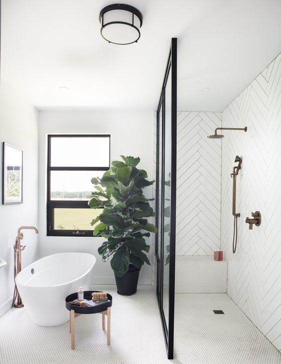 a modern white bathroom with herringbone tiles, a shower space clad with penny ones, an oval tub and a statement plant