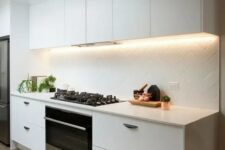 a modern white kitchen is made more eye-catchy with lights and a geometrically clad backsplash