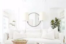 a modern white living room with a soft sofa and an ottoman, table lamps and a potted plant plus potted greenery
