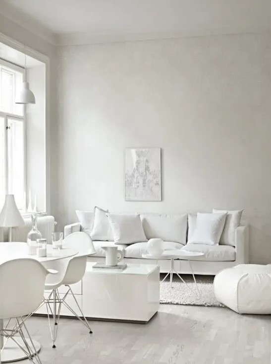 a modern white living room with chic seating furniture, a sleek white storage unit, a dining space with white furniture right here
