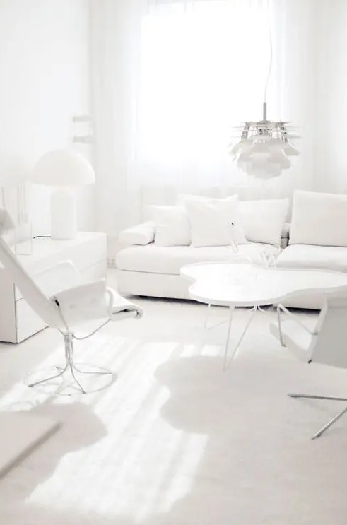a modern white living room with comfortable seating furniture, a dresser, coffee tables, a pendant lamp, all white