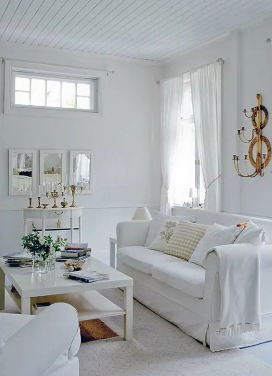 a modern white living room with much natural light, white seating furniture, a low coffee table, a delicate console table and some blooms is a chic space