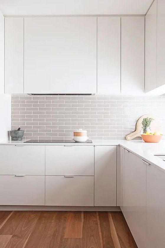 a modern white space is made more eye-catchy with a grey tile backsplash and wooden floors