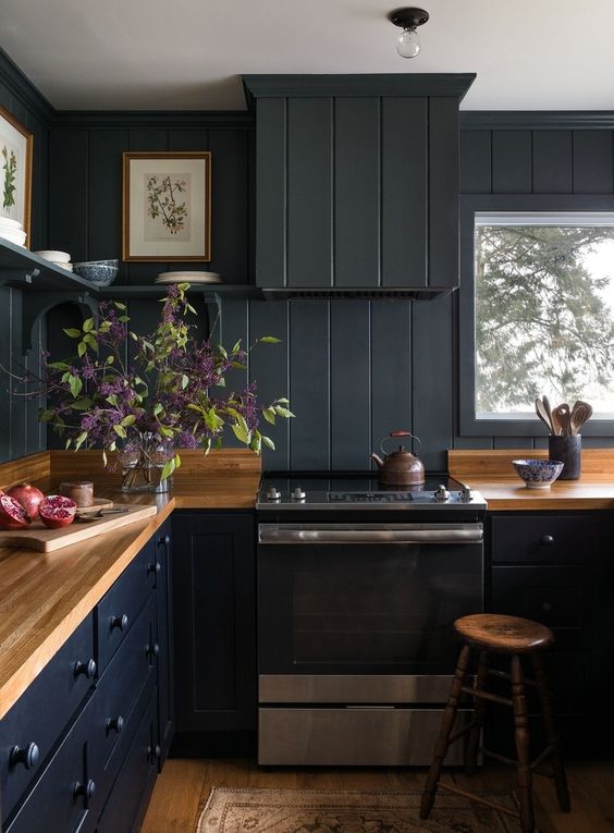 a moody black kitchen with a matching beadboard backsplash and hood, butcherblock countertops and stained stools