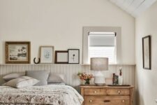 a neutral attic bedroom with a grey beadboard ceiling and walls, a vintage bed with printed bedding, some artwork