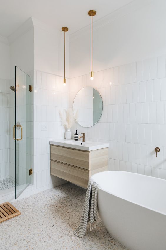 a neutral bathroom with white tiles and terrazzo, a shower and an oval tub, a floating timber vanity and a round mirror
