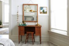 a neutral bedroom done with off-white beadboard, a vintage makeup table and a stool, a mirror in a matching frame