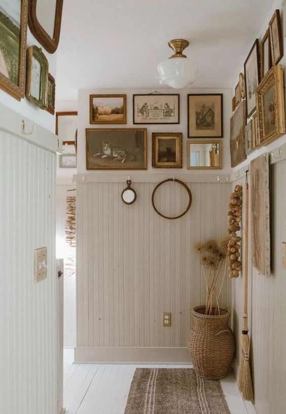 a neutral entryway with off-white beadboard on the walls, a large gallery wall everywhere, a basket and some lamps
