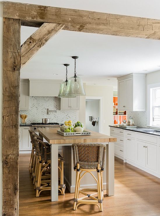 a neutral kitchen with a large kitchen island, tall stools and a rough wood wooden beam plus a pillar that brings rustic charm here
