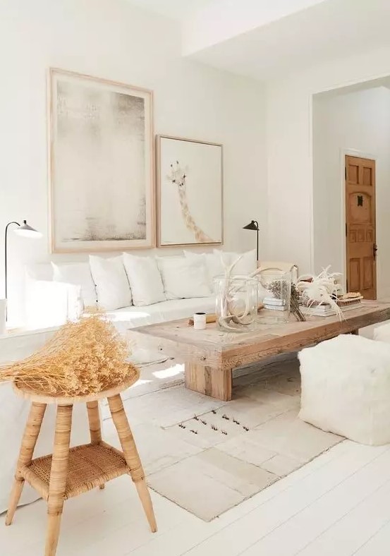 a neutral living room ith white furniture, a wooden table and stool, layered rugs, a gallery wall