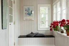 a neutral mudroom clad with beadboard, with a built-in bench, a striped rug and potted blooms