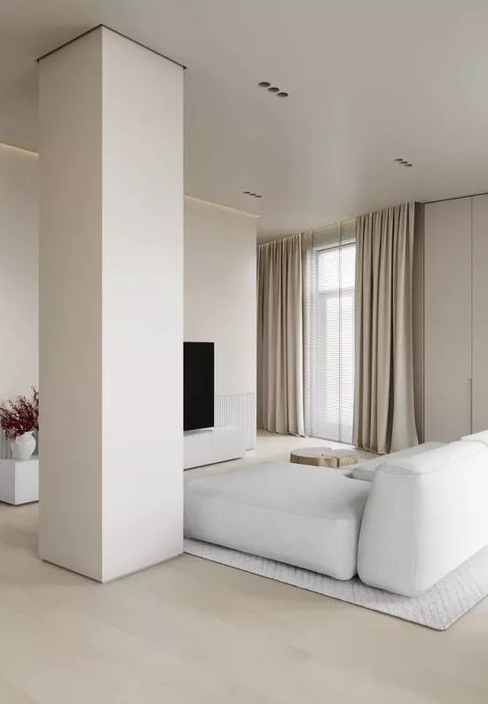 a neutral ultra-minimalist living room with a TV, a white sectional, a pillar and neutral textiles