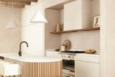 a neutral warm-colored kitchen with sleek cabinets, an open shelf, a curved and fluted kitchen island and pendant lamps