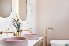 a pretty bathroom with a pink penny tile accent wall, an oval tub, a timber floating vanity, pink sinks and curved mirrors