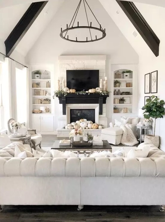 a refined neutral living room with a fireplace, a large and sophisticated tufted sofa, a chandelier, dark beams and white chairs