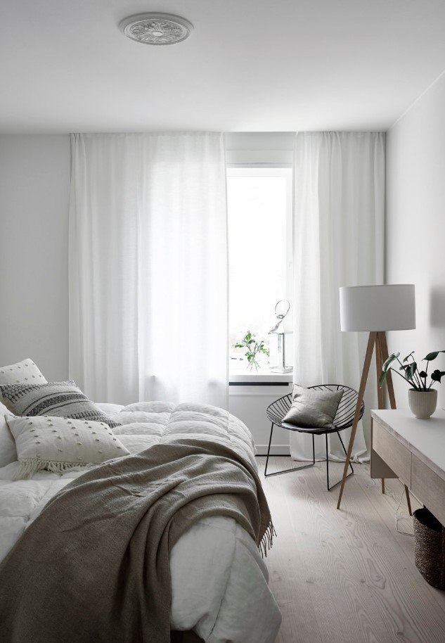 a serene and clean Scandinavian bedroom with stylish furniture, a floor lamp, a black chair and neutral bedding