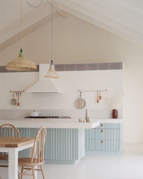 a serene coastal kitchen with light blue ribbed cabinets and a kitchen island, white countertops and woven pendant lamps