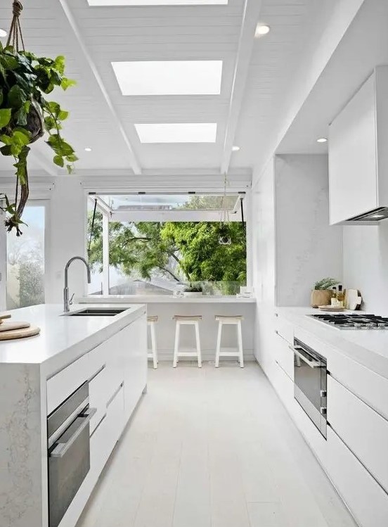 a serene white contemporary kitchen with sleek cabinets, a large kitchen island, white stone countertops and a backsplash