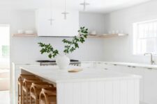 a serene white kitchen with modern cabinets, a kitchen island with wooden slatting, an open shelf and stained stools