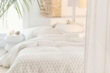 a simple white bedroom with a low bed with white bedding, a faux fur decoration, a pendant lamp and a potted plant