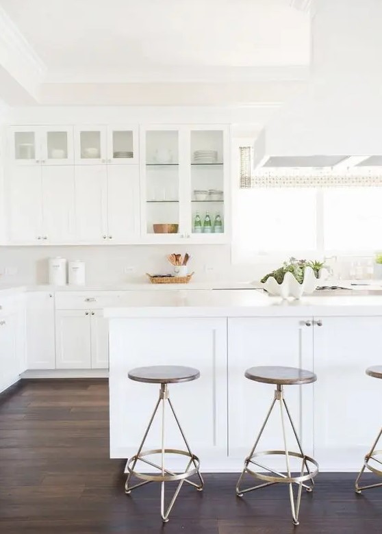 a simple white kitchen with glass cabinets and a large kitchen island leaves an airy feeling