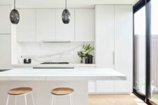 a sleek minimalist kitchen in white, with a white marble backsplash, black pendant lamps over the island and tall stools