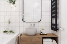 a small Scandinavian bathroom clad with white square tiles, a floating vanity, some plants and black touches for drama