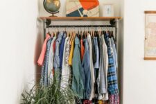a small corner makeshift closet with a metal and wood shelf, a potted plant and lots of colorful clothes plus a dresser