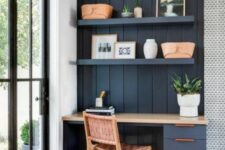 a small navy home office nook clad with beadboard, with shelves, a desk, a woven chair and some potted plants